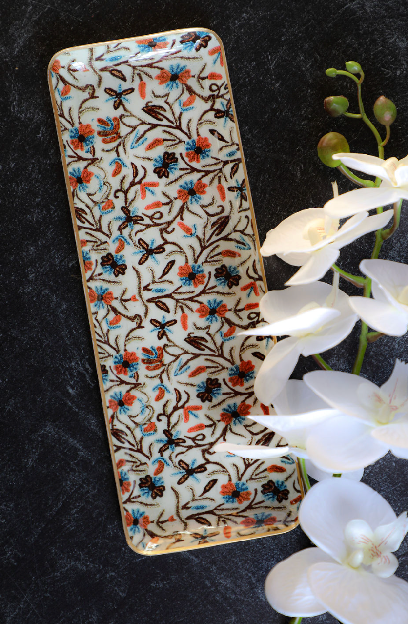 Enameled metal tray with gold rim from unknown vendor, featuring a floral pattern with white orchids.
