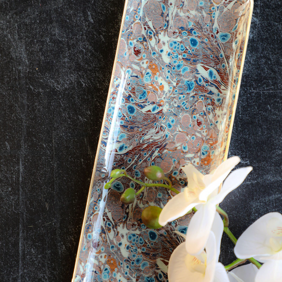 Enameled metal tray with gold rim and marbled pattern, adorned with a white orchid.
