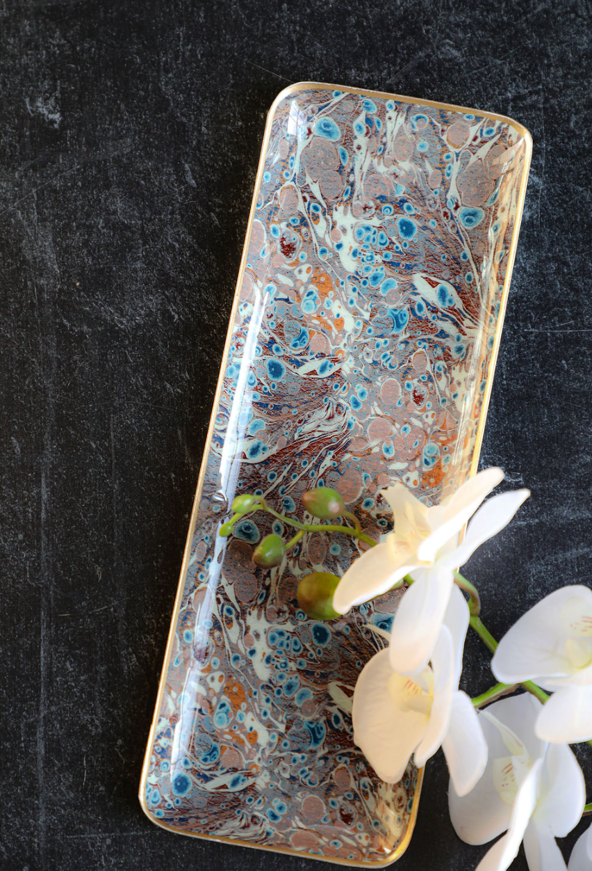 Enameled metal tray with gold rim and marbled pattern, adorned with a white orchid.
