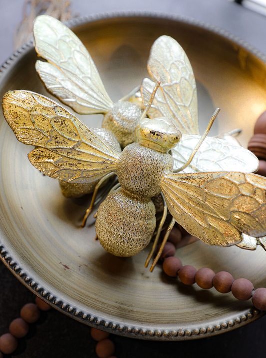 Gold finish resin bee home decor accent with intricate wing details, resting in a decorative bowl with wooden beads.