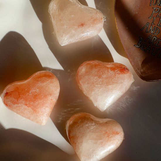 Pink Himalayan salt heart stones with a crystal-like texture, near a brown dish with a written message.