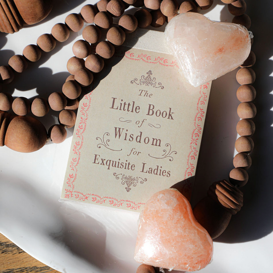 The Little Book of Wisdom for Exquisite Ladies, surrounded by a beaded necklace and heart-shaped soaps.