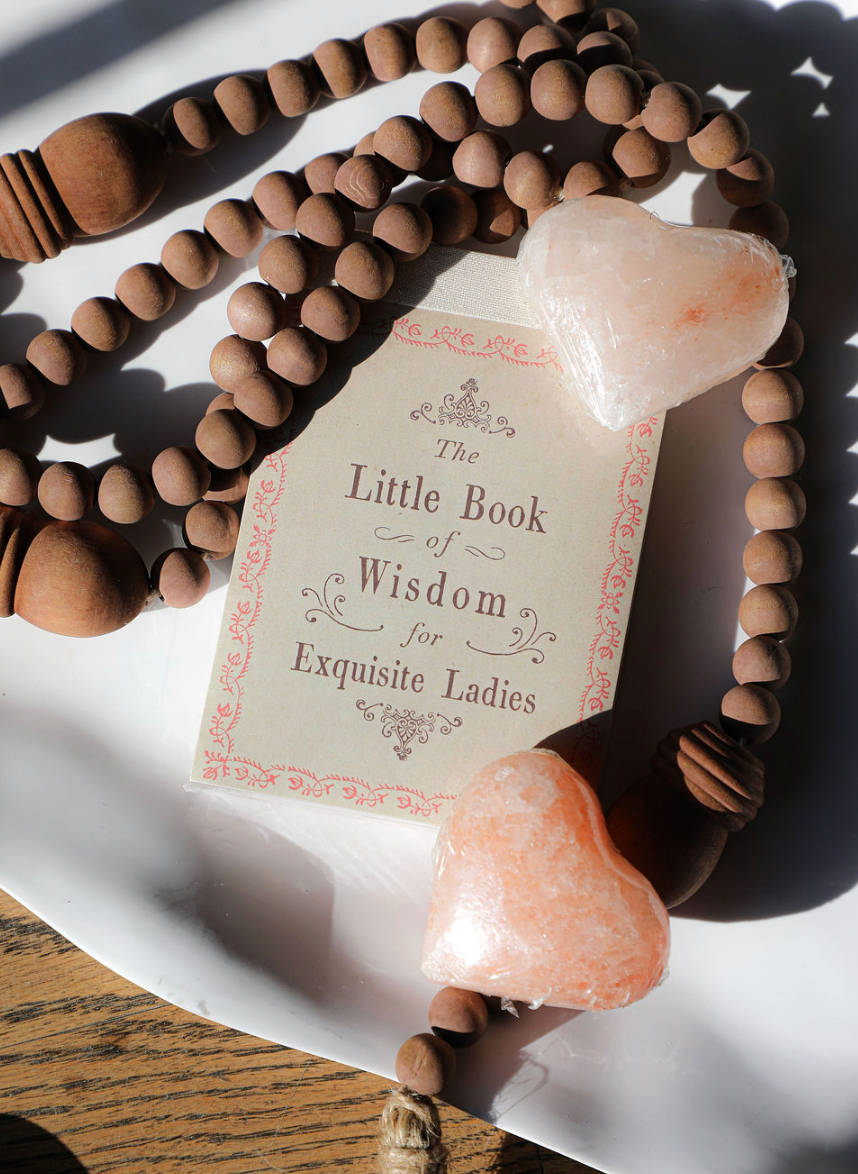 The Little Book of Wisdom for Exquisite Ladies, surrounded by a beaded necklace and heart-shaped soaps.