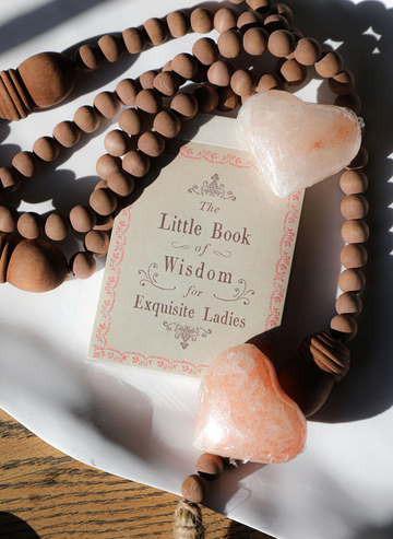 The Little Book of Wisdom for Exquisite Ladies, surrounded by a beaded necklace and heart-shaped soaps.