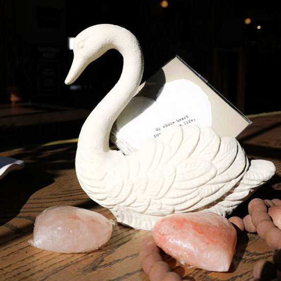 Antique white swan container of cast iron, holding a card, with decorative stones and beads.