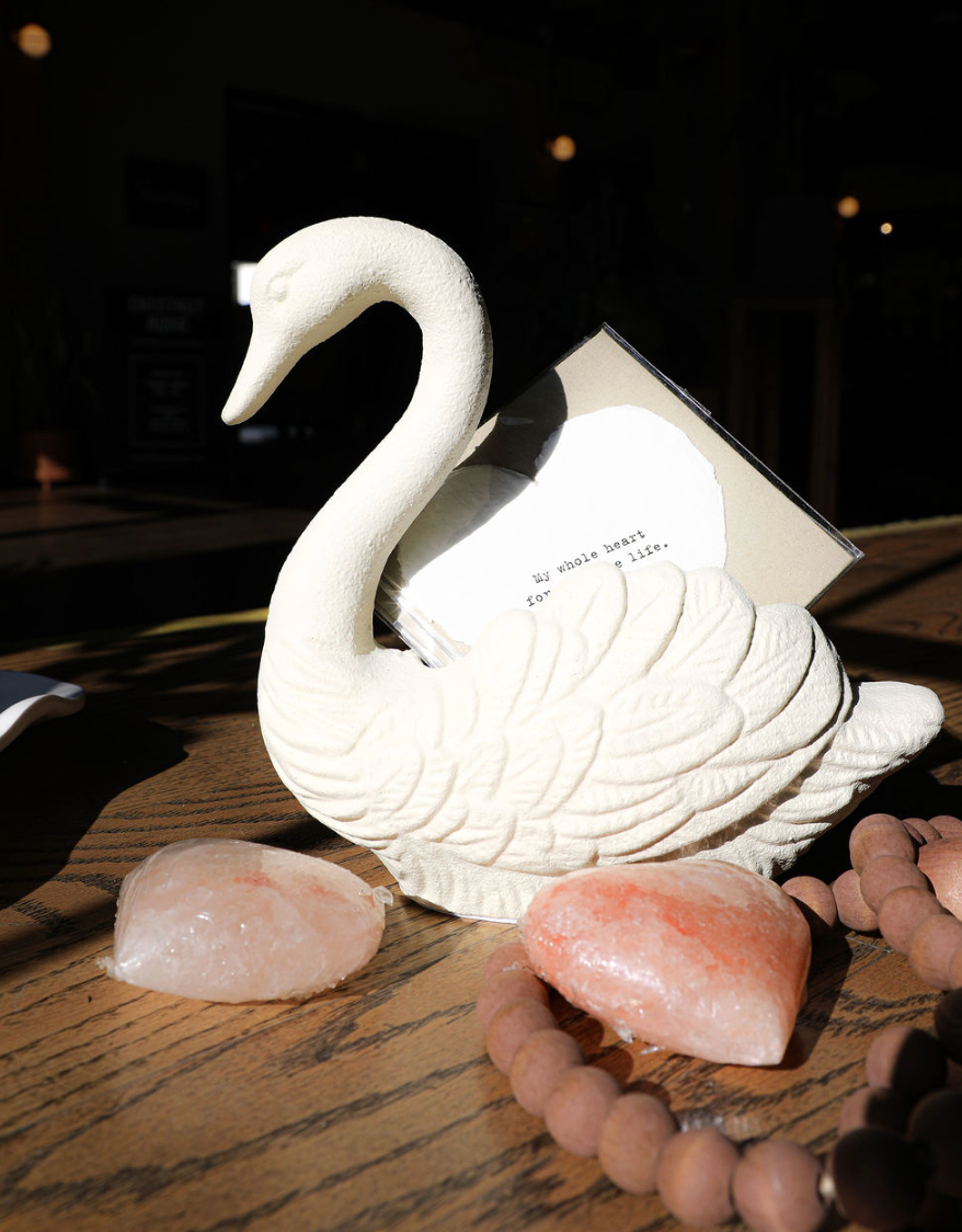 Antique white swan container of cast iron, holding a card, with decorative stones and beads.
