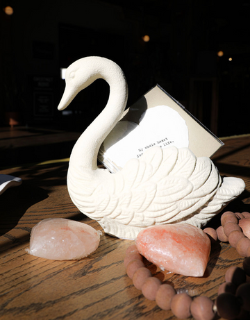 Antique white swan container of cast iron, holding a card, with decorative stones and beads.