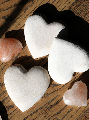 Carved wooden heart by an unknown brand, arranged with pink salt hearts on a wooden table.