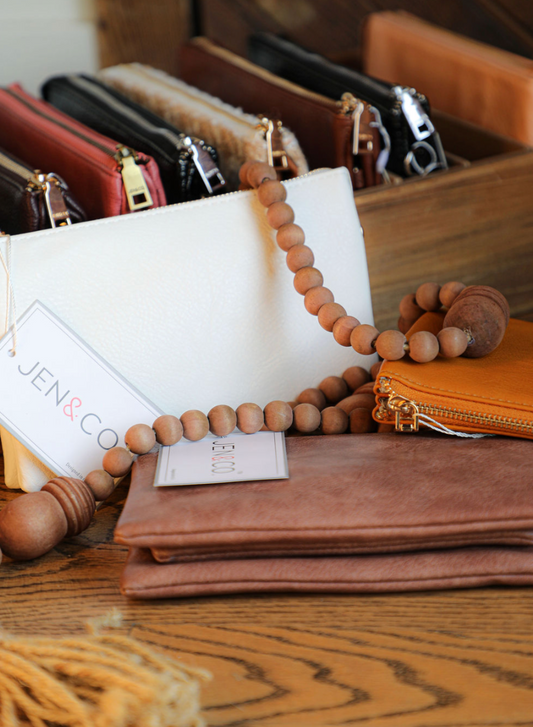 Vegan leather wristlet by Jen&Co, with a wooden beaded strap and multiple zipper pouches.