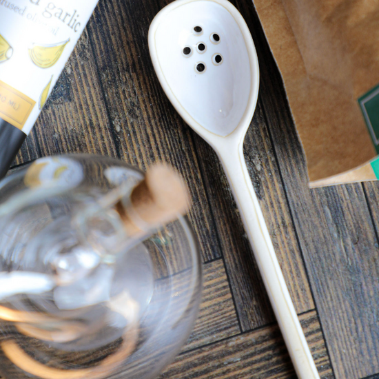Small white stoneware strainer by Mud Pie with six drainage holes, laying on a rustic wooden surface.

