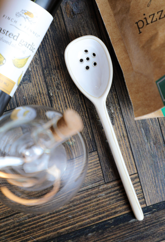 Small white stoneware strainer by Mud Pie with six drainage holes, laying on a rustic wooden surface.
