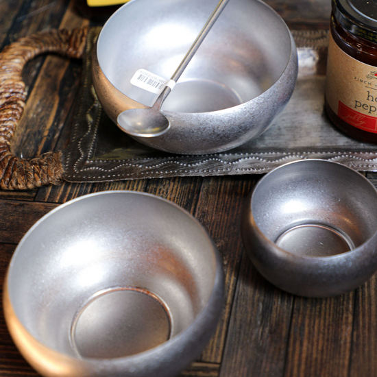 Set of three stainless steel nesting bowls by unknown vendor, with a spoon on a decorative tray.