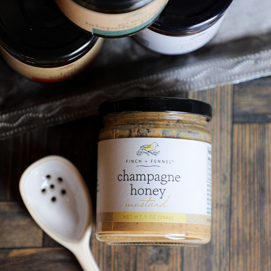 Gourmet champagne honey mustard by Finch + Fennel with a serving spoon on a wooden surface.
