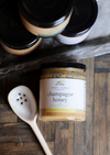 Gourmet champagne honey mustard by Finch + Fennel with a serving spoon on a wooden surface.
