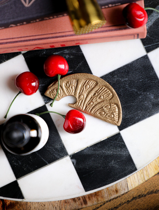 Gold metal lemon slice shaped bottle opener with textured details on a black and white checkered surface with cherries.
