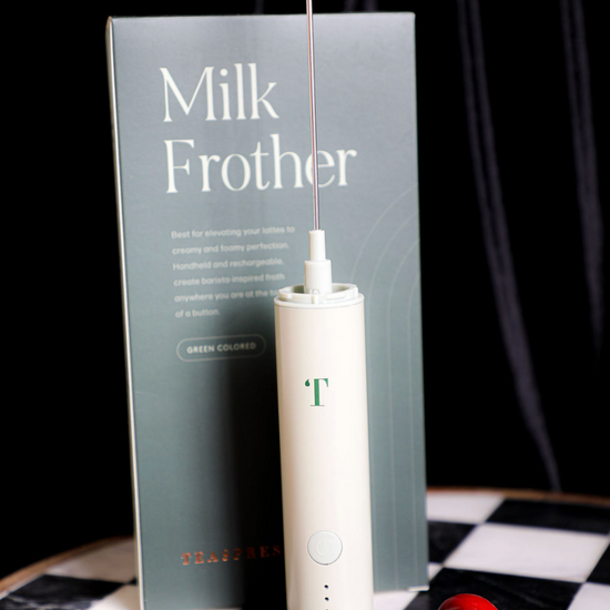 Pistachio milk frother by Teaspressa with a silver whisk attachment and a box, displayed with ripe cherries.
