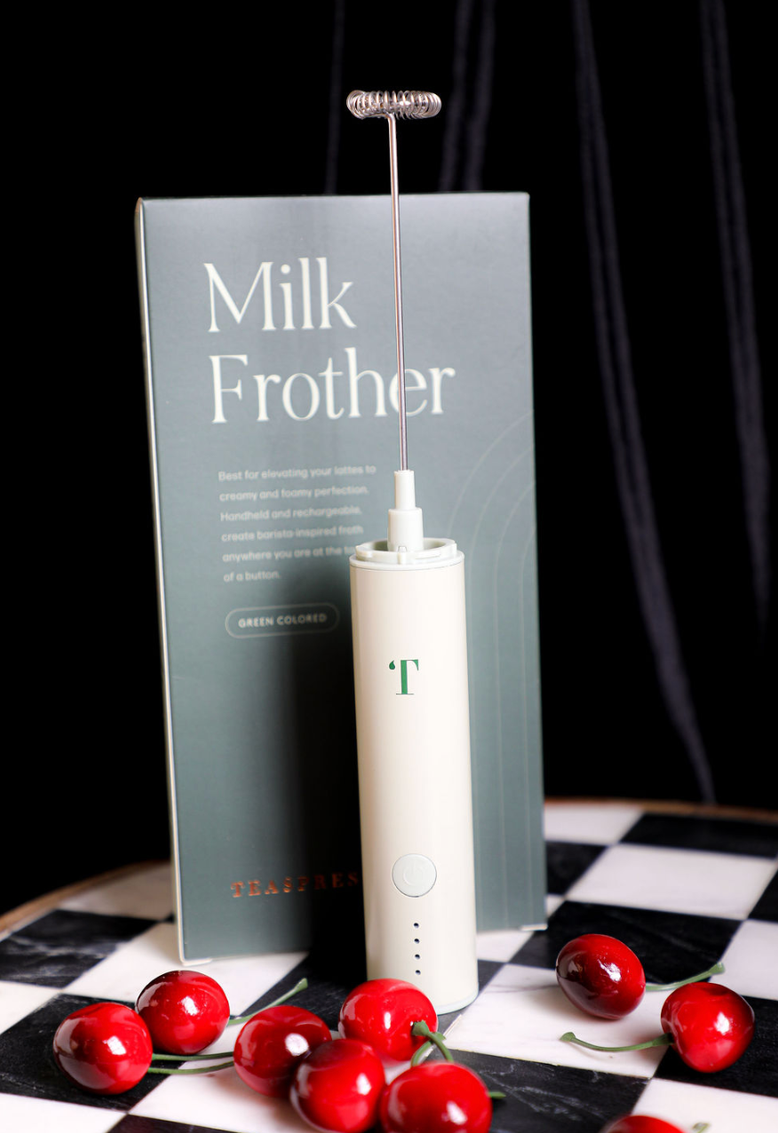 Pistachio milk frother by Teaspressa with a silver whisk attachment and a box, displayed with ripe cherries.
