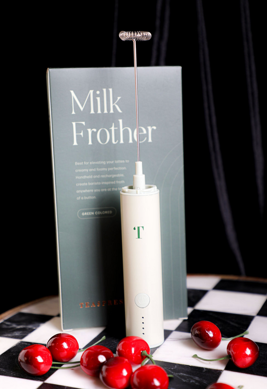 Pistachio milk frother by Teaspressa with a silver whisk attachment and a box, displayed with ripe cherries.
