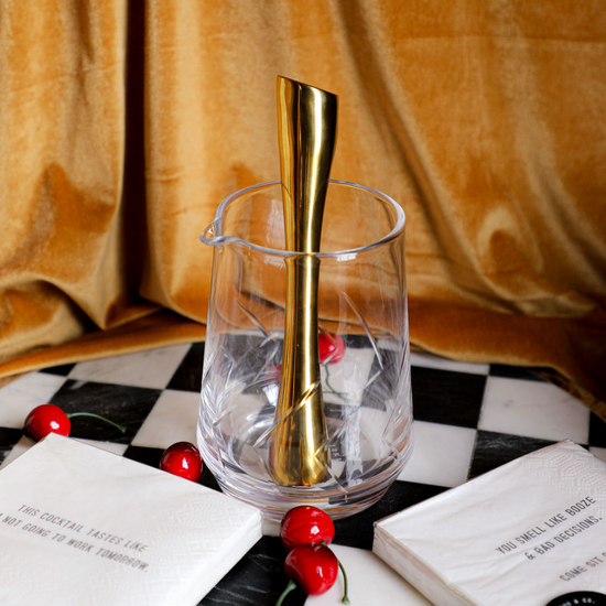 Clear cocktail mixing glass with golden bar spoon, by Burke, with cut crystal pattern, cherries and cocktail napkins.