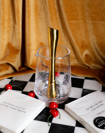 Clear cocktail mixing glass with golden bar spoon, by Burke, with cut crystal pattern, cherries and cocktail napkins.