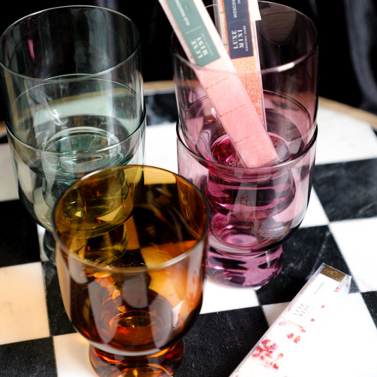 Colored drinking glasses by an unknown brand displayed on a black and white checkered surface.

