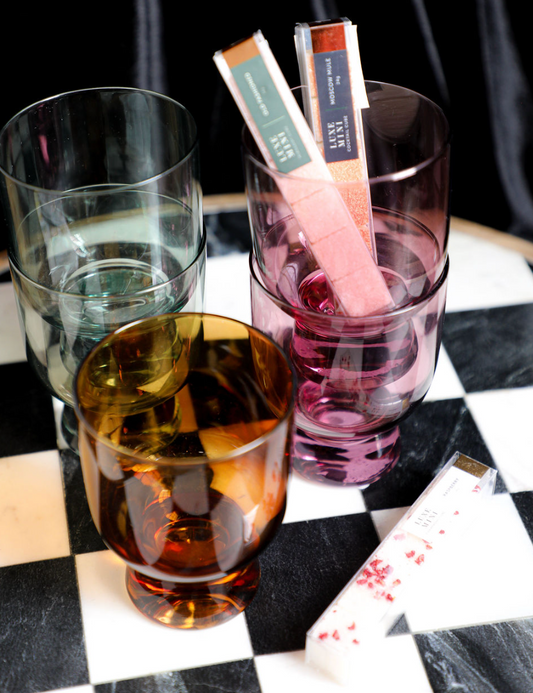 Colored drinking glasses by an unknown brand displayed on a black and white checkered surface.
