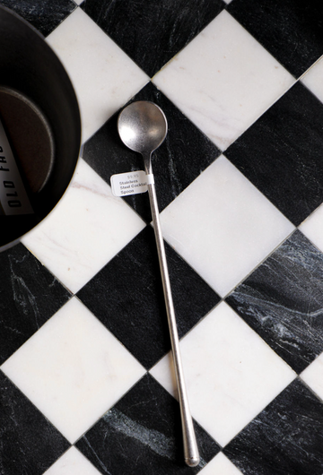 Stainless steel cocktail spoon from Unknown Vendor, lying on a black and white checkered surface.