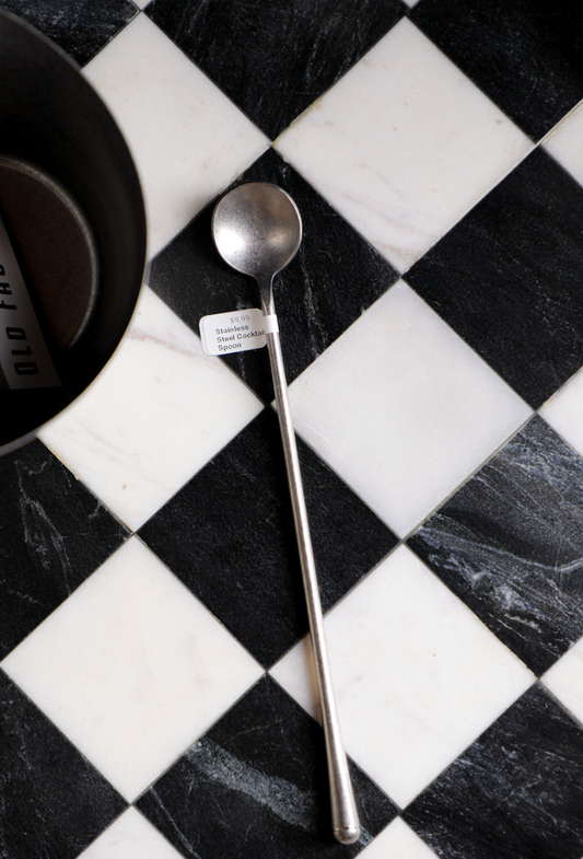 Stainless steel cocktail spoon from Unknown Vendor, lying on a black and white checkered surface.