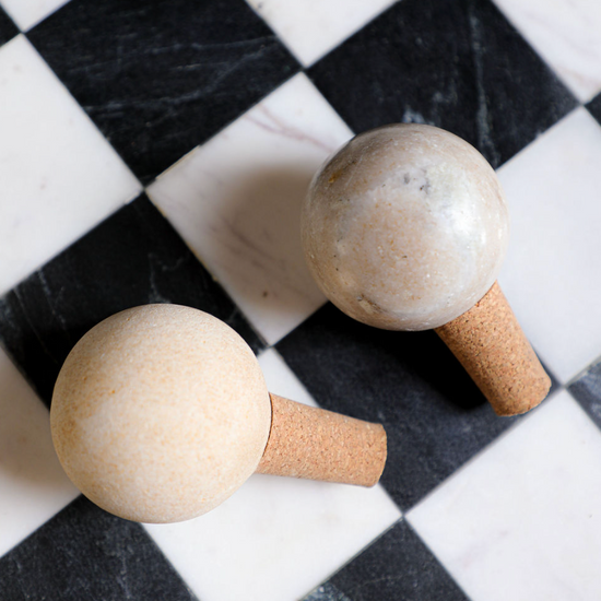 Two marble and cork bottle stoppers on a black and white checkered surface.

