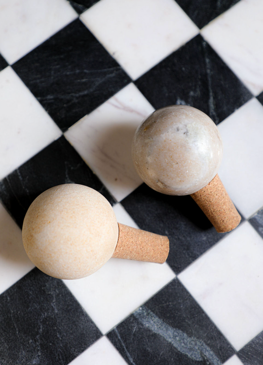 Two marble and cork bottle stoppers on a black and white checkered surface.
