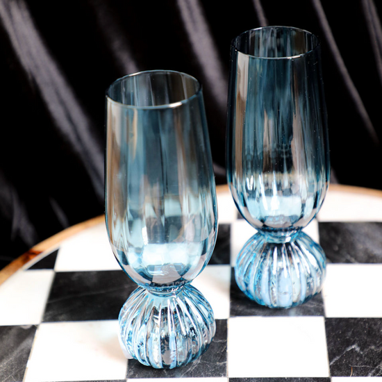 Blue pleated footed champagne glasses by unspecified brand, on a chessboard.