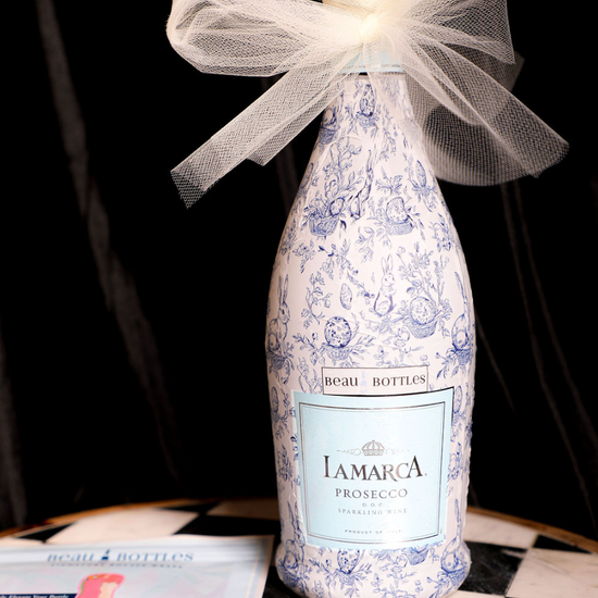 Wrapped prosecco bottle by Beau Bottles with a blue and white floral pattern and a white tulle bow.