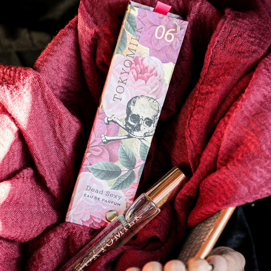 Travel spray fragrance by Tokyo Milk, showcased with its packaging amidst draped burgundy fabric and wooden beads.
