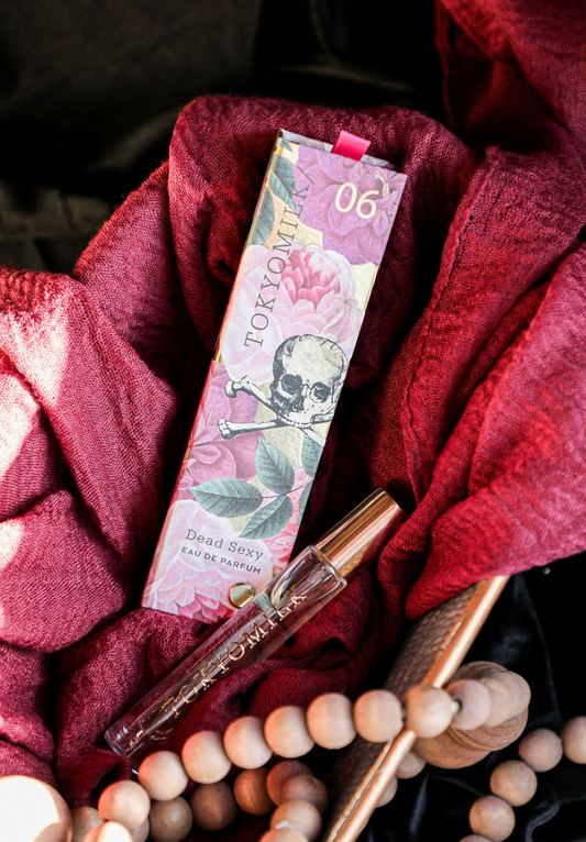 Travel spray fragrance by Tokyo Milk, showcased with its packaging amidst draped burgundy fabric and wooden beads.
