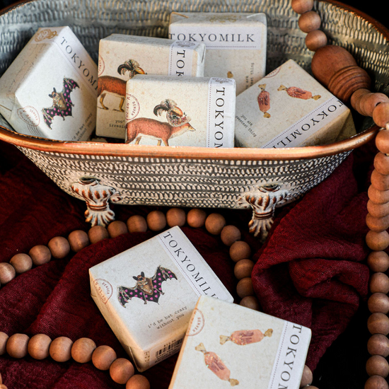 Scented soaps by Tokyo Milk in decorative vintage packaging, displayed in a rustic metal basket with beaded garland and red fabric.
