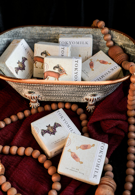 Scented soaps by Tokyo Milk in decorative vintage packaging, displayed in a rustic metal basket with beaded garland and red fabric.
