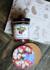Jar of raspberry jam by Finding Home, with a black and white checkered label, on a colorful floral coaster.
