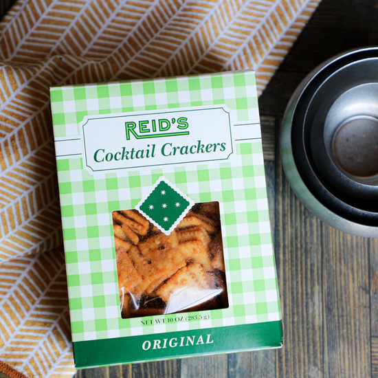 Box of cocktail crackers by Reid's, displayed near a dish towel with a geometric pattern.
