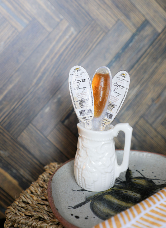 Unfiltered clover honey filled single use spoons by Finch & Fennel in a decorative pitcher.