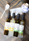 Gourmet barrel aged balsamics and infused olive oils from Finch + Fennel, arranged on a wooden surface with a white spoon and recipe card.
