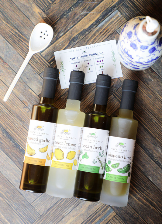 Gourmet barrel aged balsamics and infused olive oils from Finch + Fennel, arranged on a wooden surface with a white spoon and recipe card.
