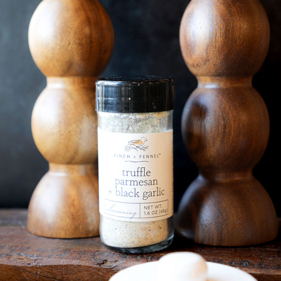Truffle parmesan and black garlic seasoning by Finch and Fennel, displayed in front of wooden decorations.
