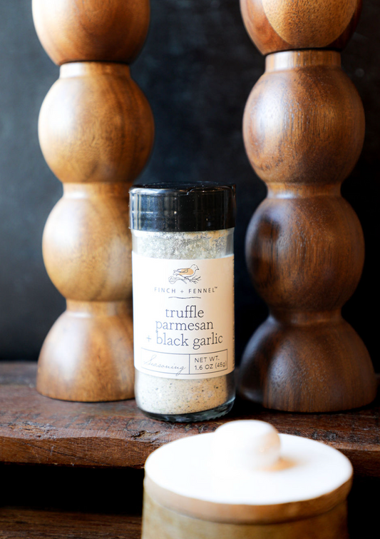 Truffle parmesan and black garlic seasoning by Finch and Fennel, displayed in front of wooden decorations.
