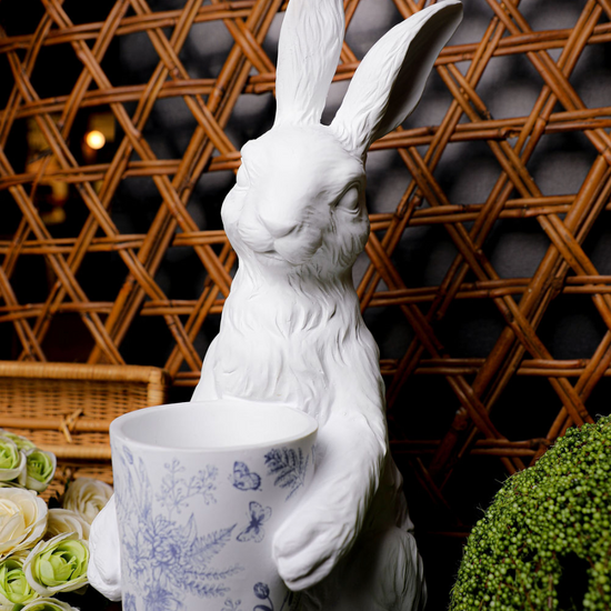 White bunny statue with floral patterned pot, in blue and white, with wicker background.