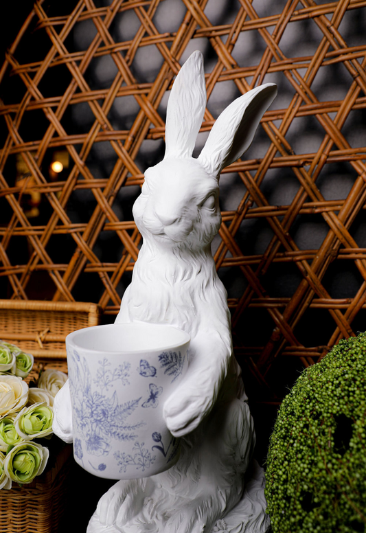 White bunny statue with floral patterned pot, in blue and white, with wicker background.