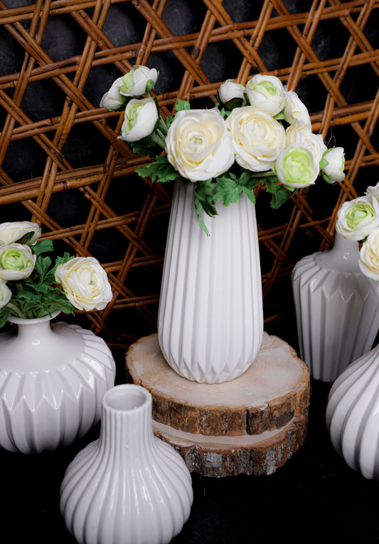 White porcelain accordion vase by Benzara, featuring a vertically ribbed texture and floral arrangement on a wooden stand.