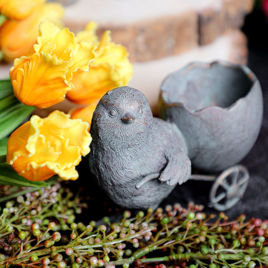 Resin chick with egg cart by Foreside Home and Garden, alongside yellow tulips and green berry sprigs.