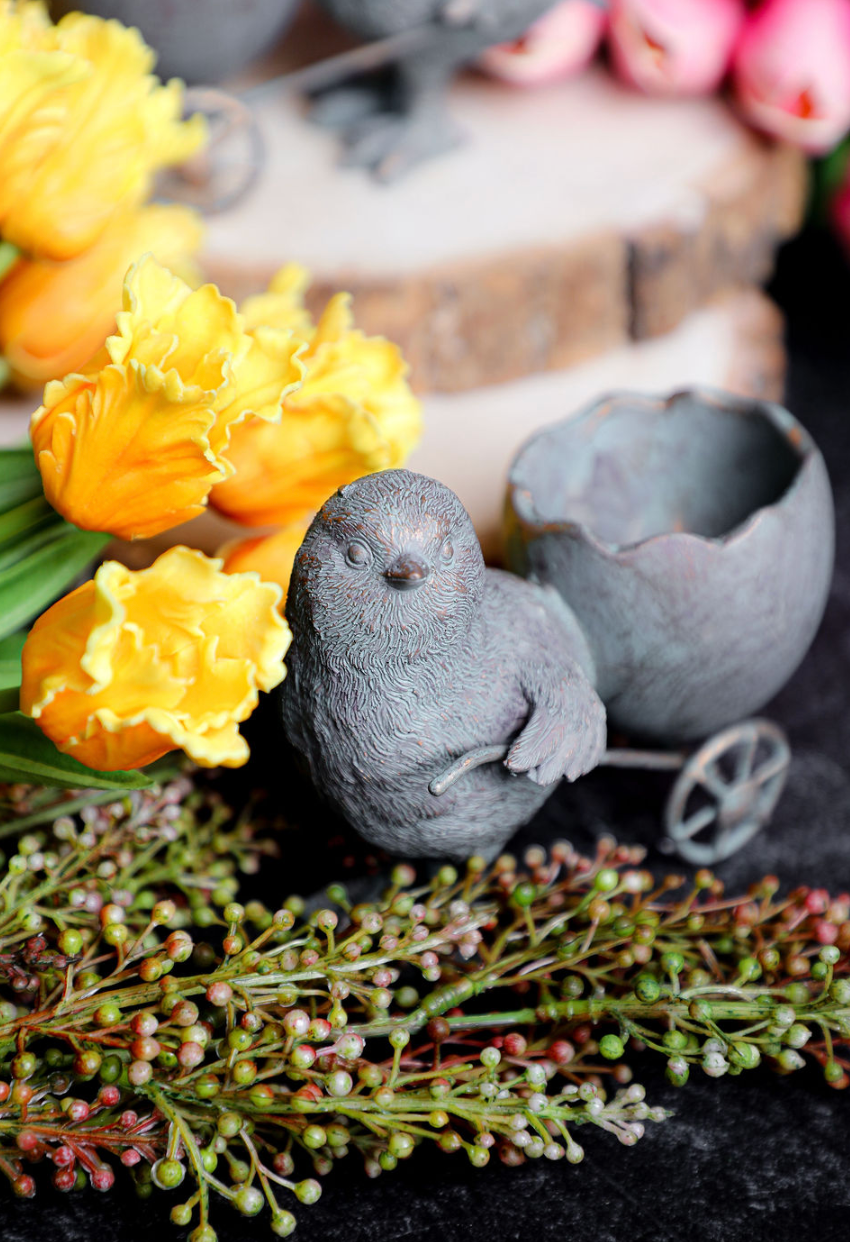 Resin chick with egg cart by Foreside Home and Garden, alongside yellow tulips and green berry sprigs.