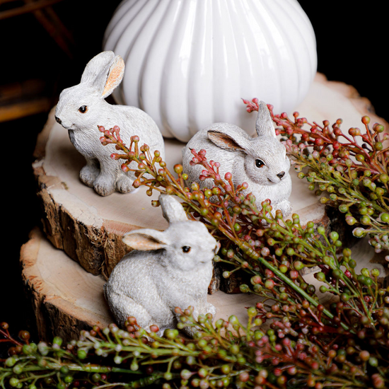 Small gray bunnies on a wood slice, surrounded by faux red berry sprigs.