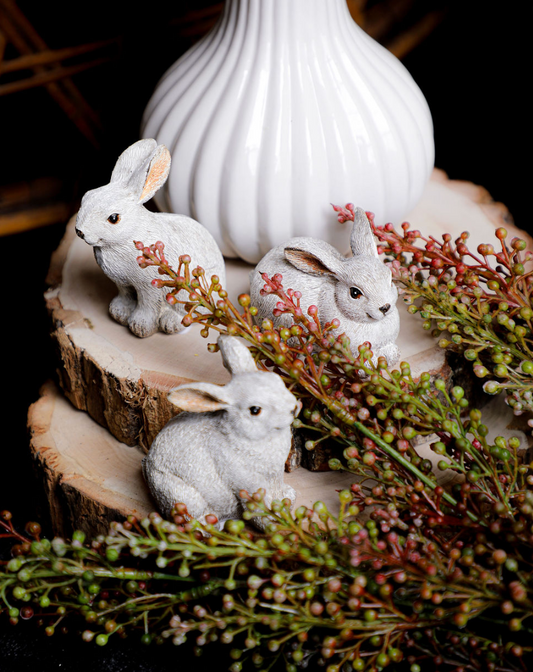 Small gray bunnies on a wood slice, surrounded by faux red berry sprigs.